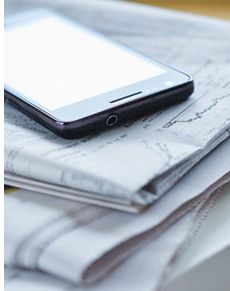 Image of a cell phone on top of a stack of folded newspapers. Digital Native vs Digital Immigrant.