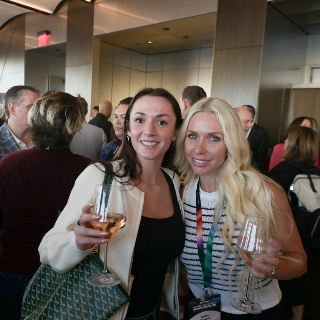 Three delegates with drinks at an evening reception, a crowd behind them.