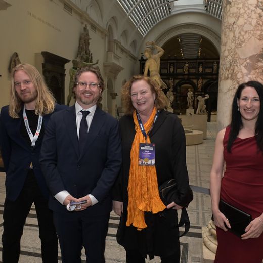 Four delegates standing together under the arches of a columned hall.
