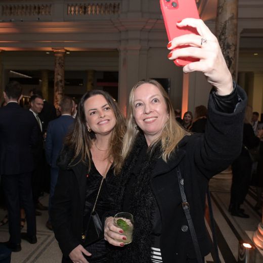 Two delegates leaning in for a selfie at a reception.