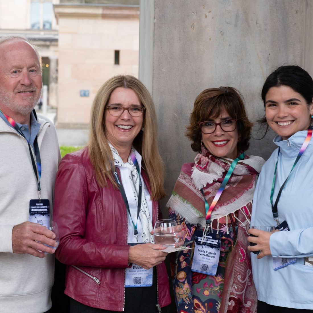 Four delegates with conference badges outside a stone building in daylight.