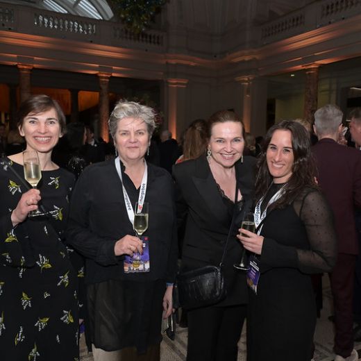 Five delegates with drinks at a reception in a columned hall.
