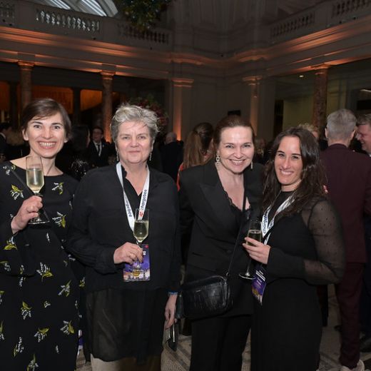 Four delegates raising glasses at a reception in a columned hall.