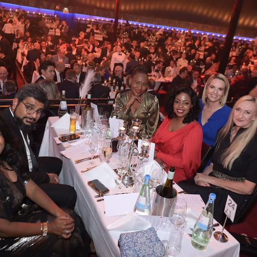 Guests at dinner tables in a darkened hall under stage lighting.