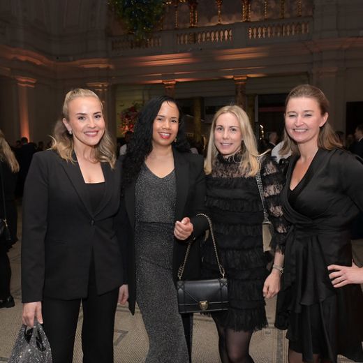Four delegates with drinks at a reception in a columned hall.