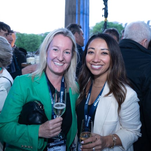 Two delegates with drinks outdoors among trees.