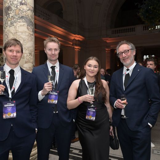 Four delegates raising glasses in a columned hall.