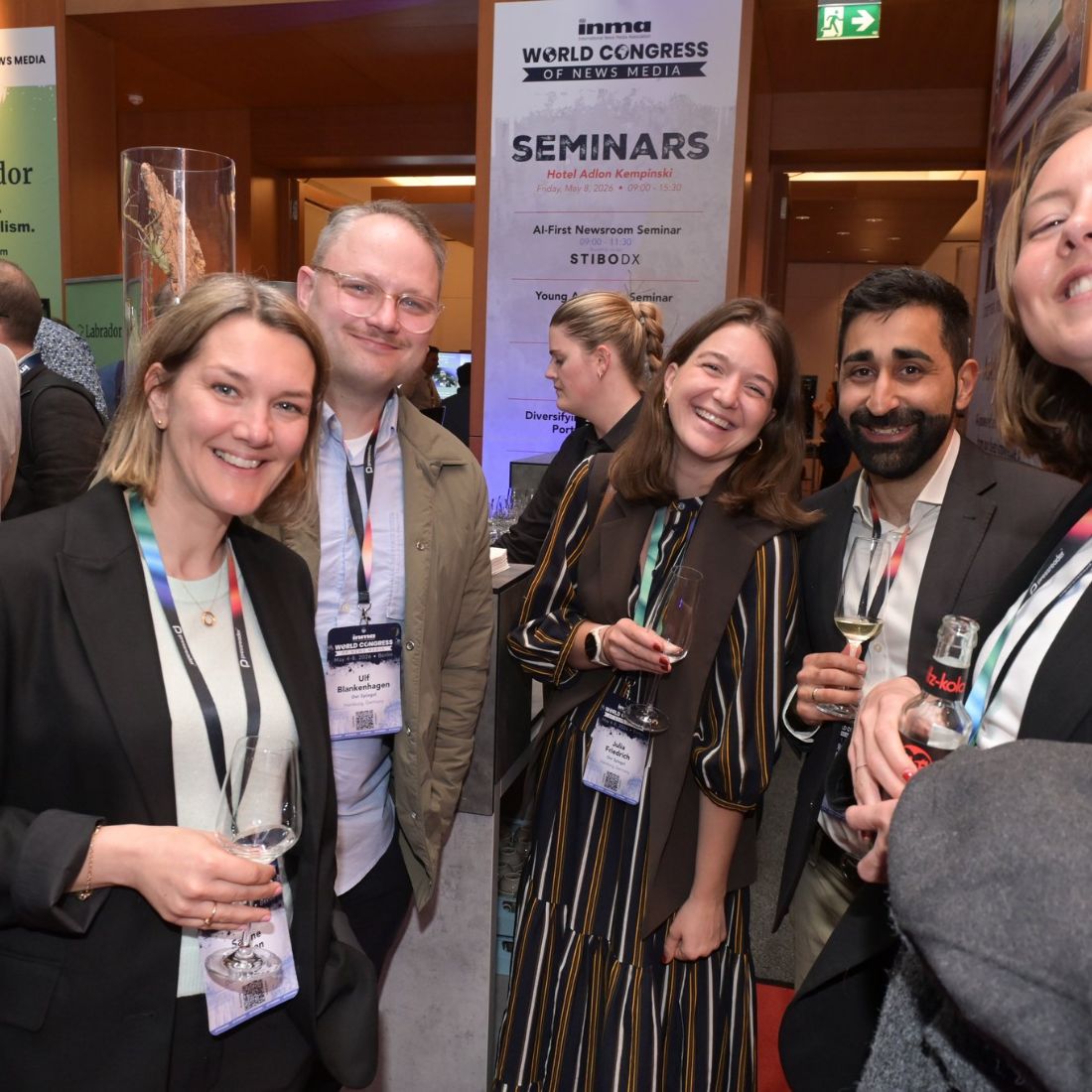 Five delegates laughing together on the conference floor, a seminars sign behind them.