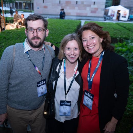 Three delegates with badges outdoors in a garden beside a marquee.