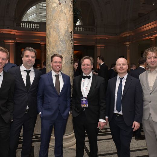 Five delegates in evening dress in a columned hall.