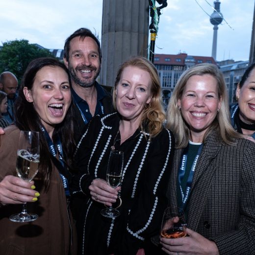 Four delegates with drinks outdoors at dusk, a lit landmark behind them.