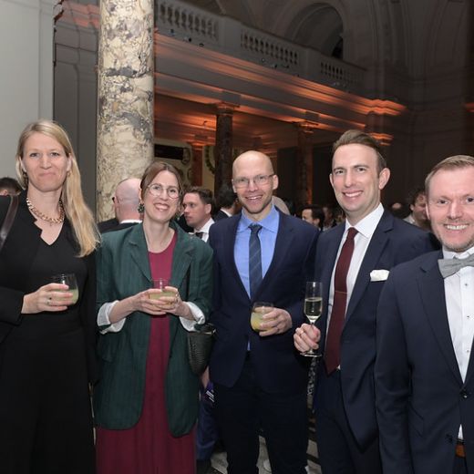 Five delegates with drinks at a reception in a columned hall.