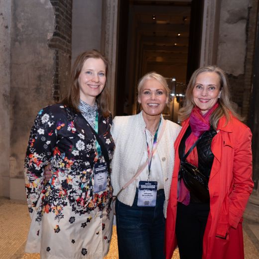 Three delegates with drinks in a columned hall.