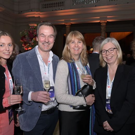 Five delegates with drinks at a reception in a columned hall.