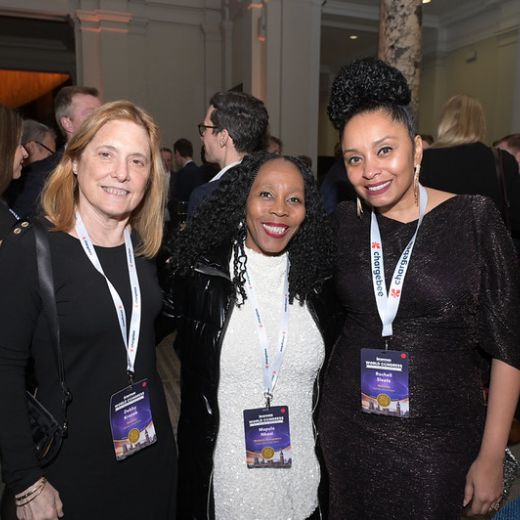 Three delegates with drinks at a reception in a columned hall.