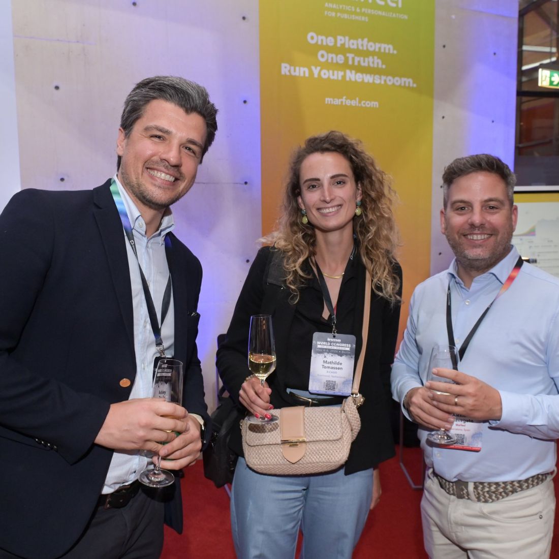 Three delegates with drinks in front of a lit conference backdrop.