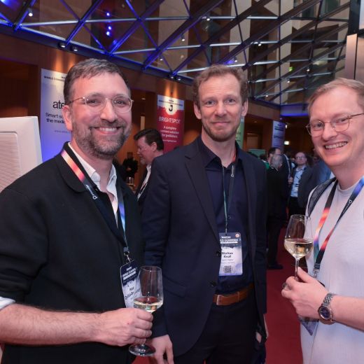 Three delegates with wine glasses under blue lighting.