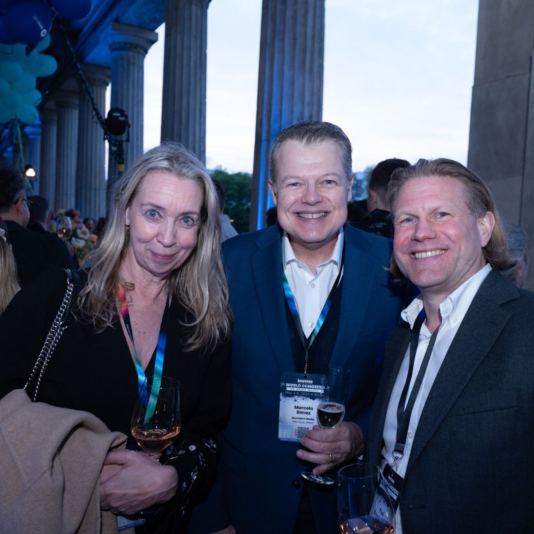 Three delegates with drinks in a columned foyer.