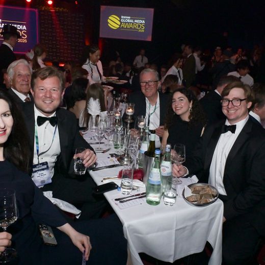 Guests around a table at the Global Media Awards dinner, the awards screen behind them.